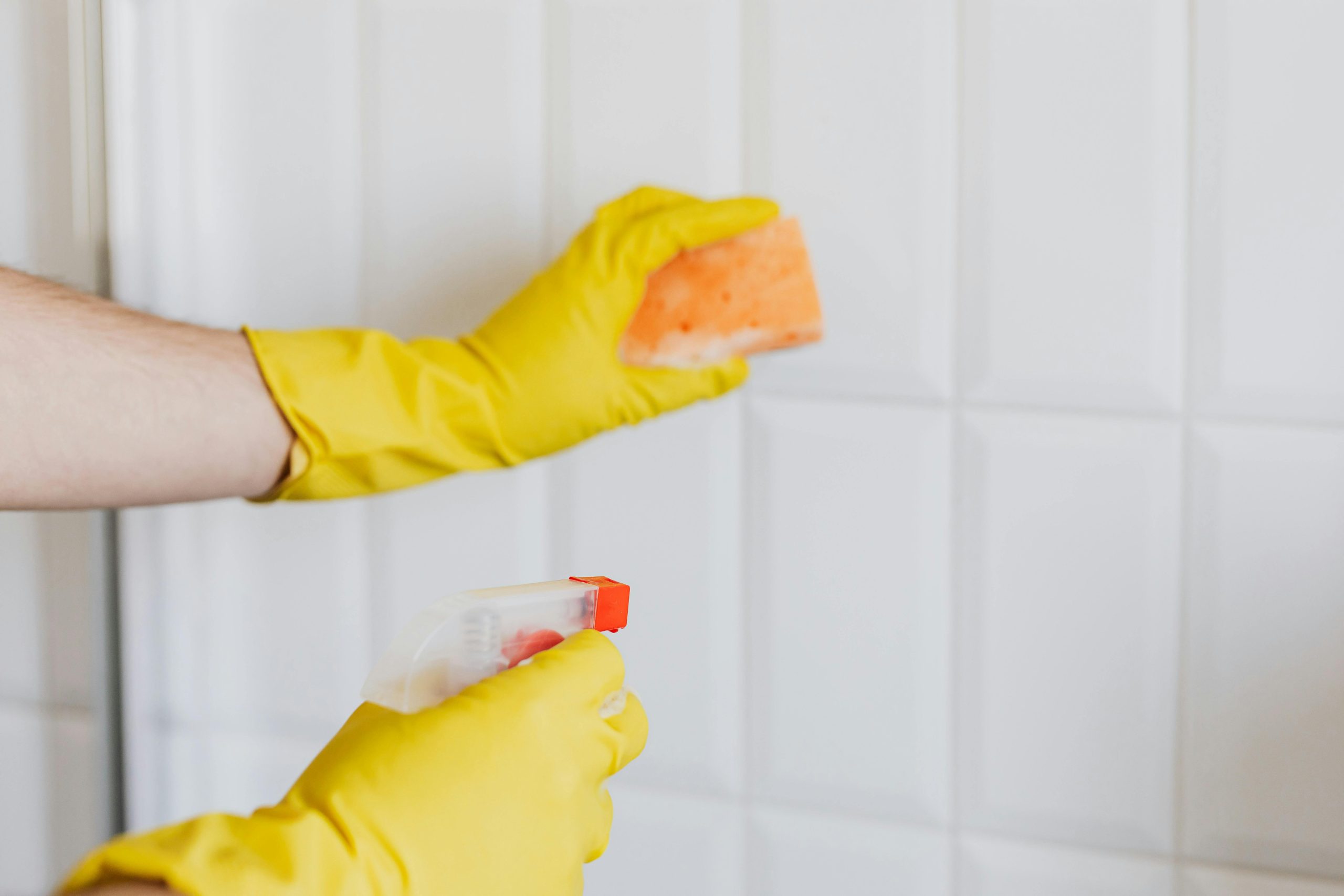 close-up of hands in yellow rubber gloves cleaning bathroom grout